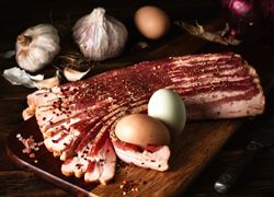 Plátky údenej slaniny na lopári s vajíčkami, cesnakom a cibuľou