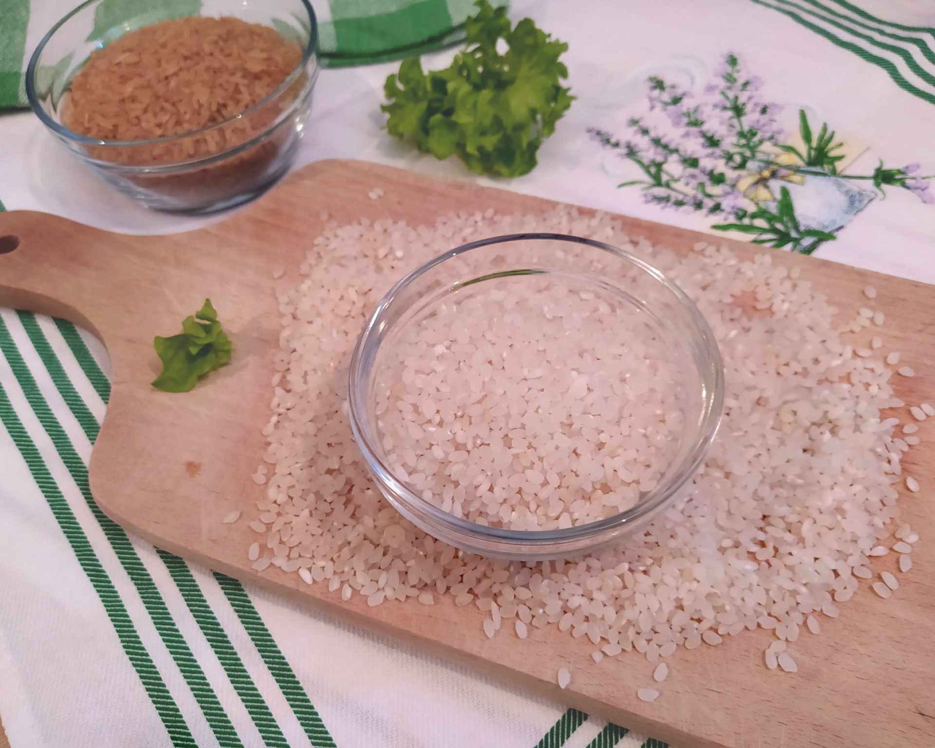 Biela ryža v sklenenej miske na drevenej doske, hnedá ryža v miske v pozadí