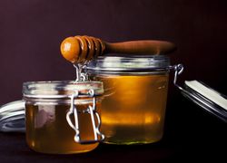 Dva poháriky s medom - jeden väčší, druhý menší - obidva zatváracie, s drevenou okrúhlou naberačkou na med