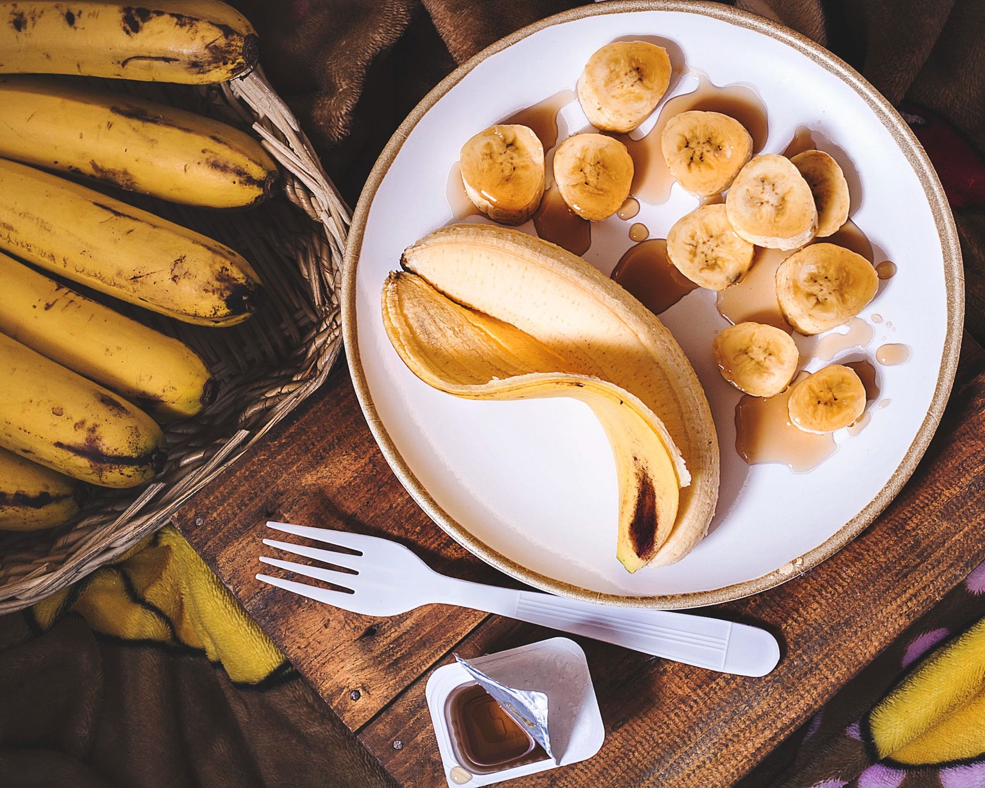 Celý olúpaný banán so šupkou a nakrájaný na kolieska na bielom tanieri, v pozadí neolúpané celé banány
